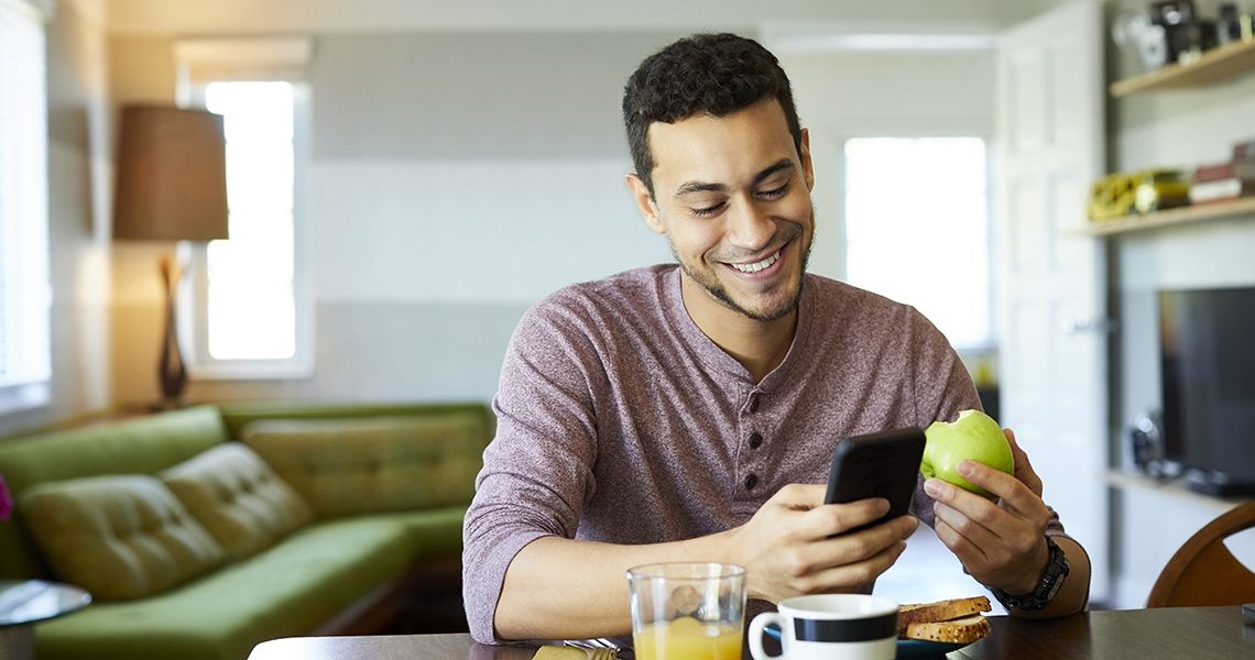 Man holding and looking at a mobile phone, eating an apple.