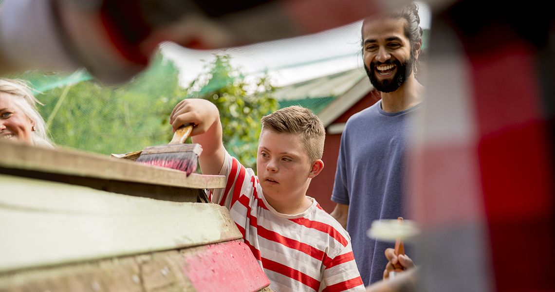 Young boy painting a wooden structure with a man behind him smiling