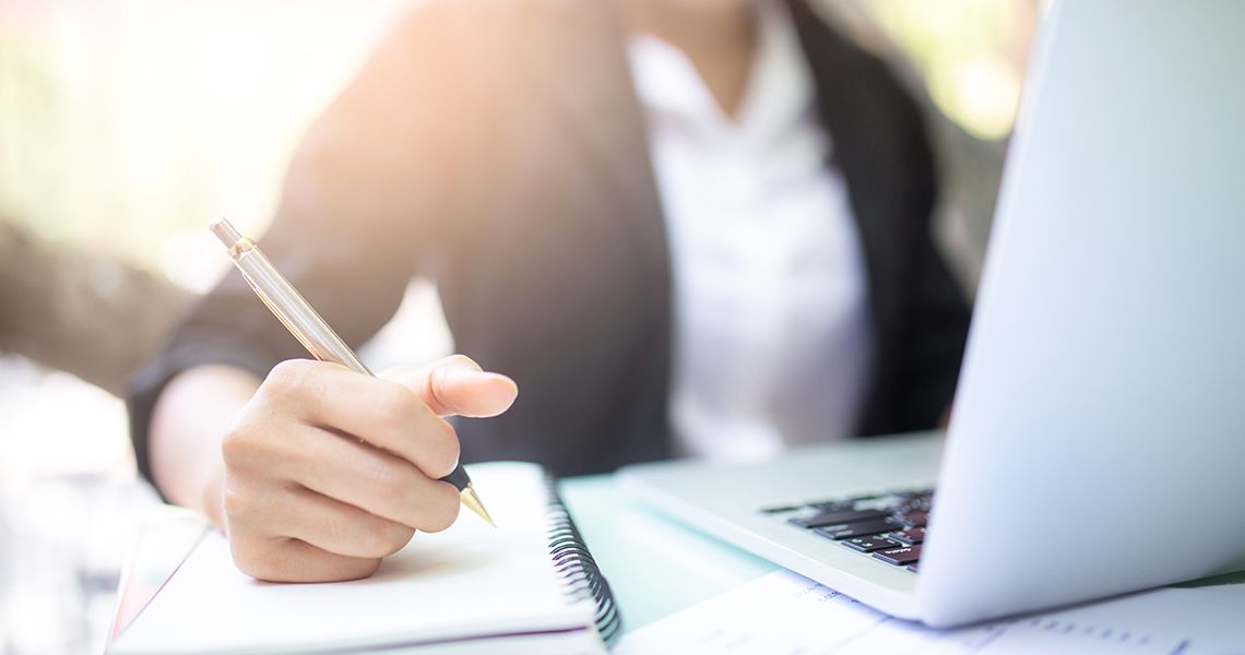 Close up of hand writing in a notebook, next to a laptop