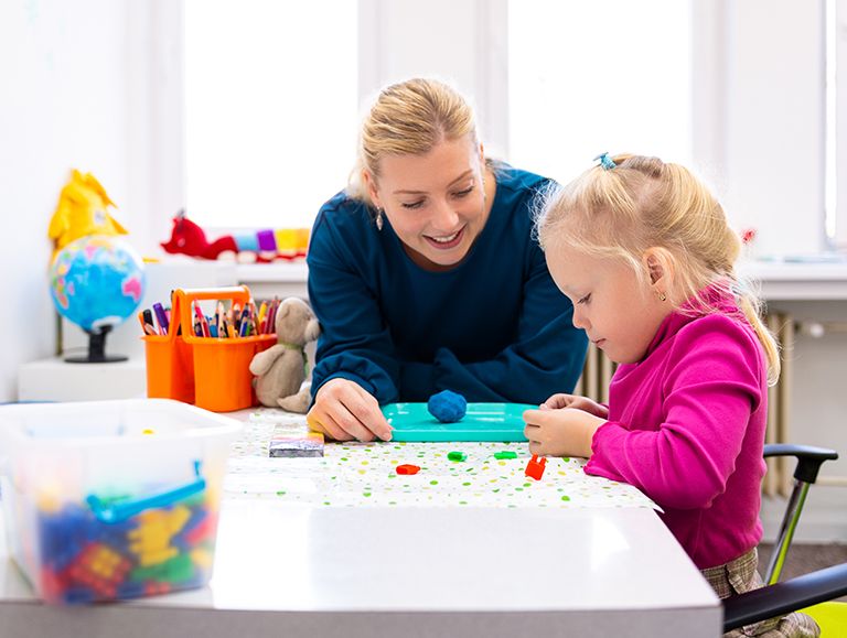 Woman helping a toddler girl play with legos