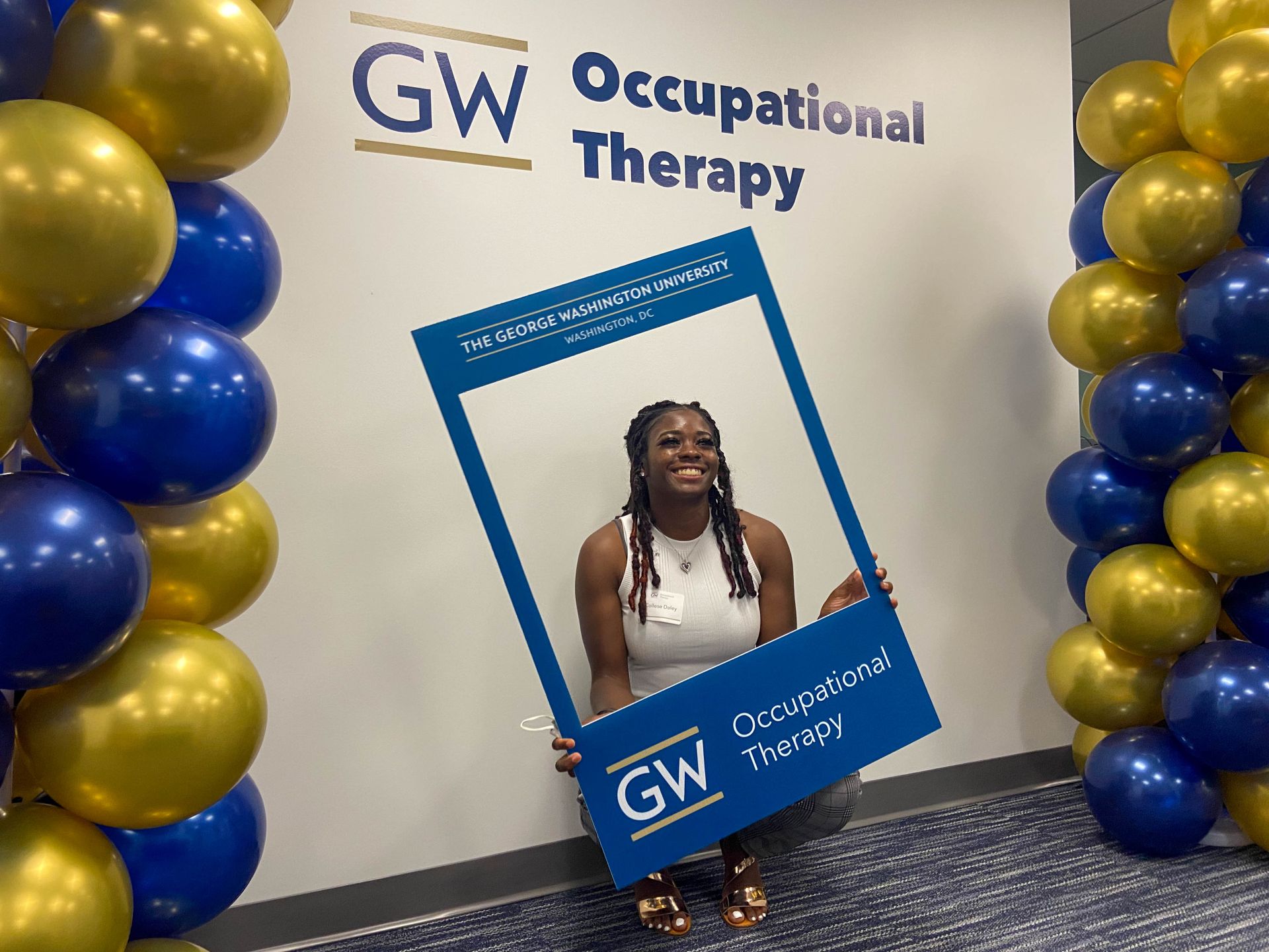 Student with picture frame sign in front of GW OT logo sign