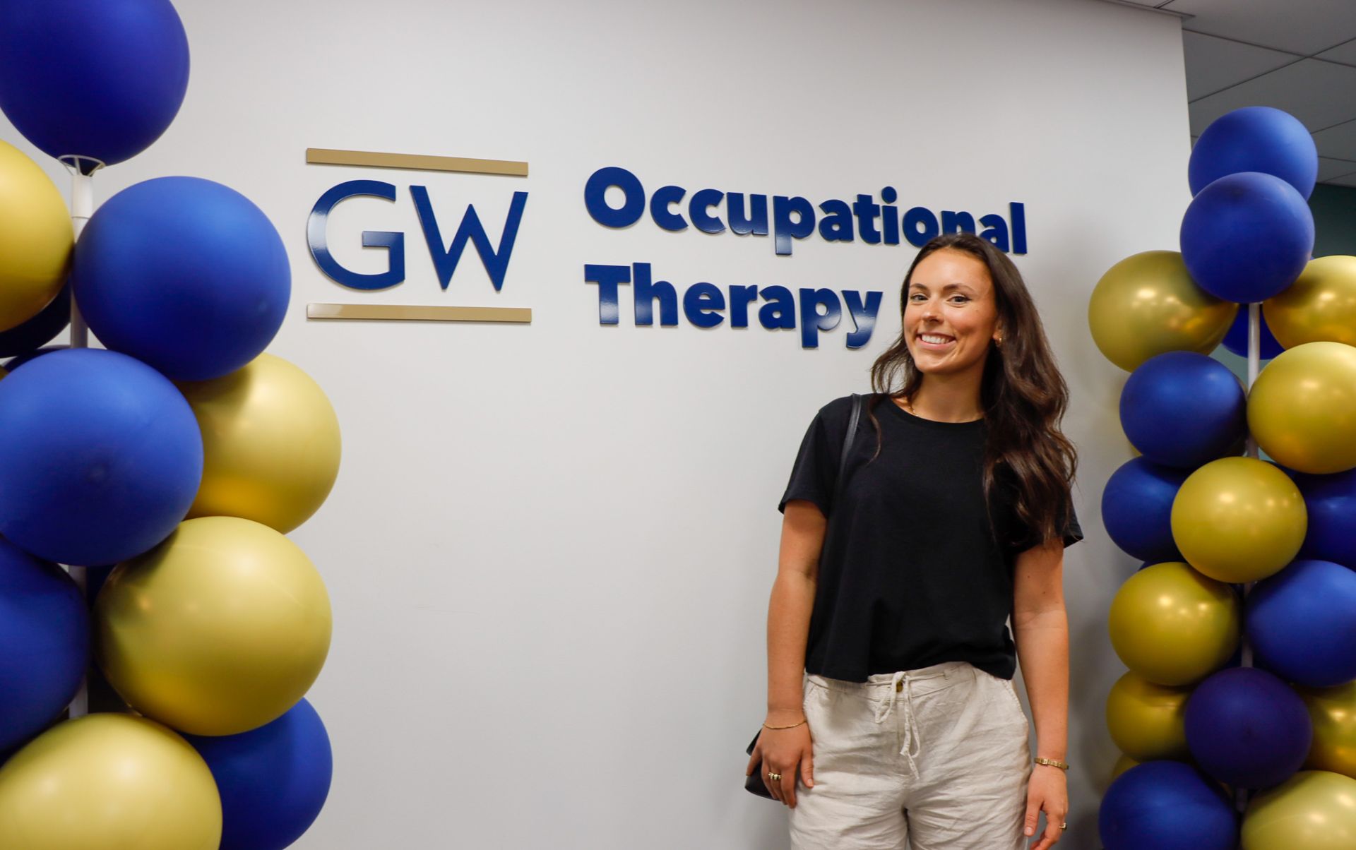 student smiling in front of GW OT sign and balloons