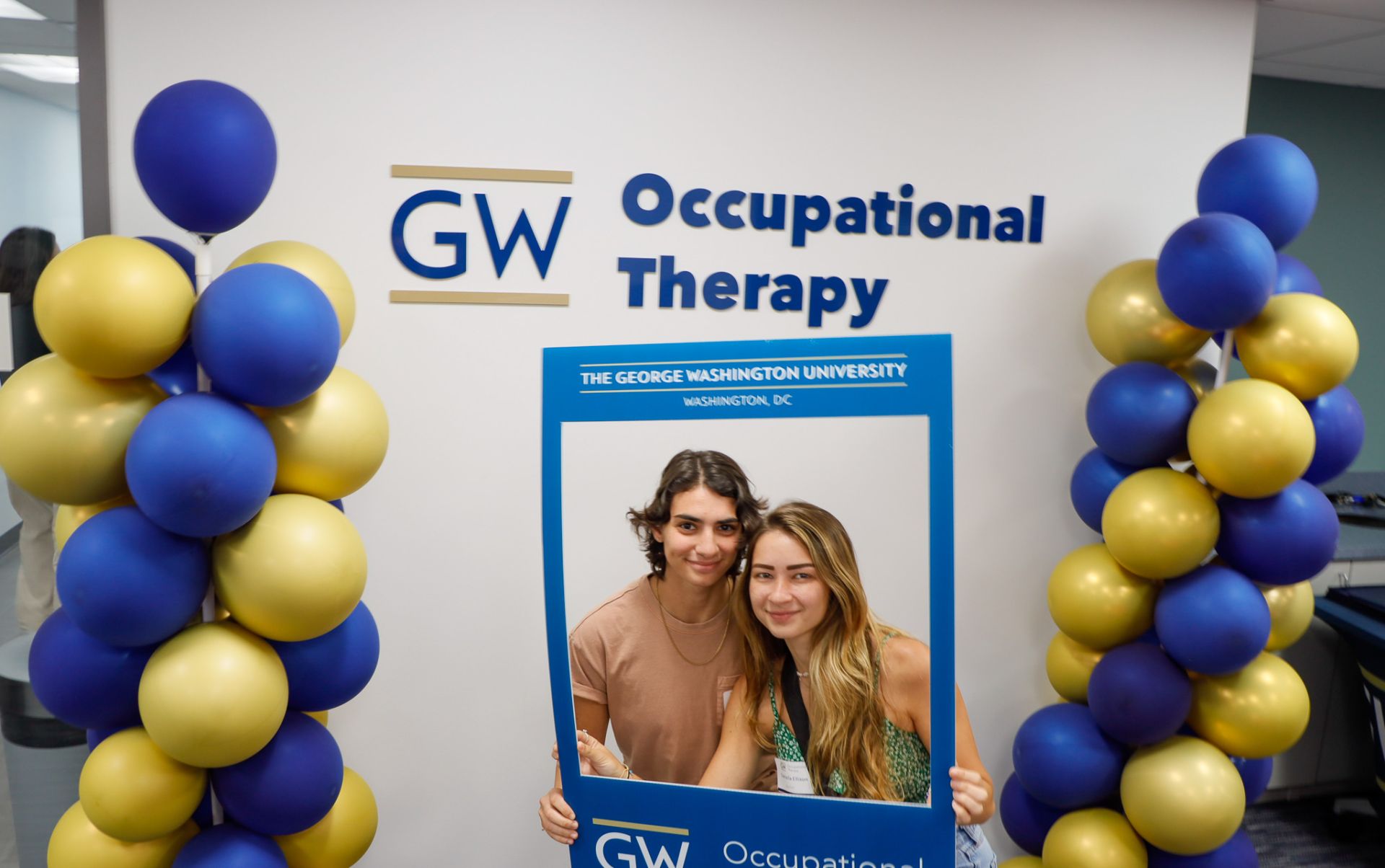 student and friend in front of GW OT sign and balloons