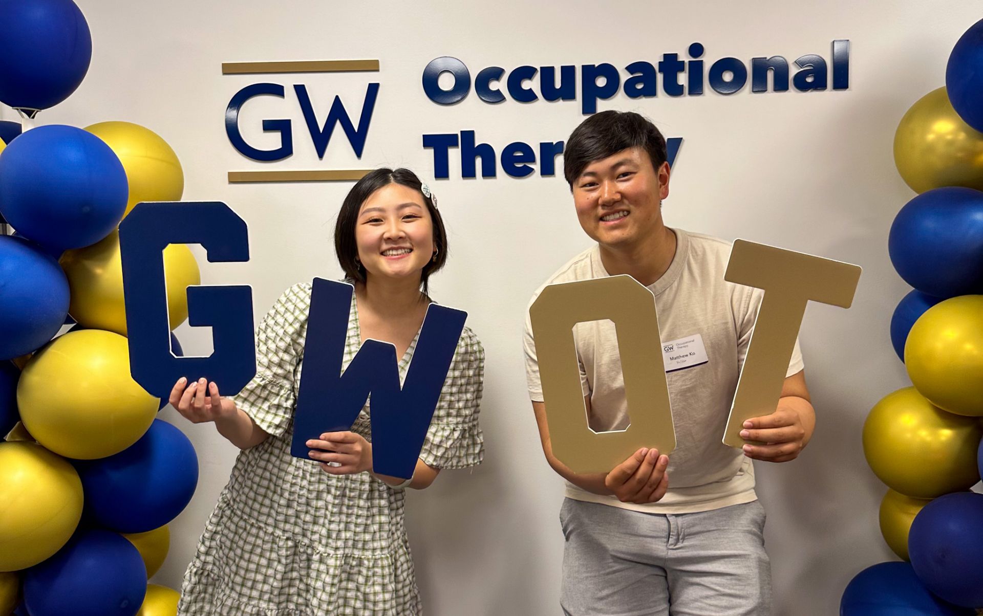 student and friend holding GW OT letters smiling in front of sign